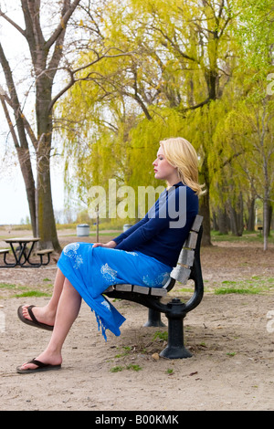 Eine schöne junge Frau sitzt auf einer einsamen Bank im Wald Stockfoto