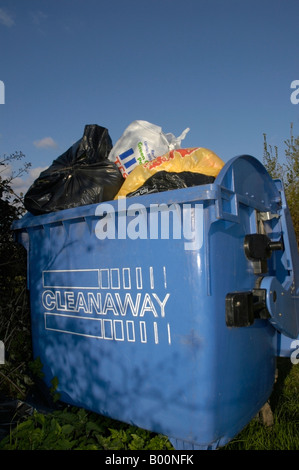 Blaue kommerzielle Wheelie bin überfüllt mit Plastiktüten Müll sitzen in einem ländlichen Layby mit einem klaren blauen Himmel 1/3 Stockfoto