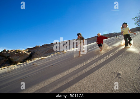 Namibia, Erongo Region Brandberg Mountain. Ein Gruppe junger Freunde heruntergekommen die Steilwand einer Sanddüne kicking Sand. Stockfoto