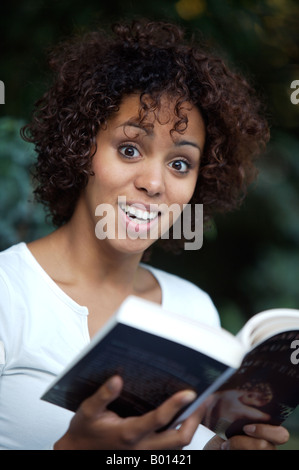 Mulata Mädchen - halb Deutsche halb kubanischen - in einem Park sitzt und liest ein Buch Stockfoto