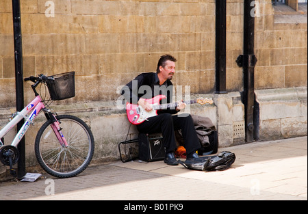 Mann, Busker, spielt e-Gitarre, Straßenmusik, sitzen durch eine Wand in Cambridge, England, UK Stockfoto