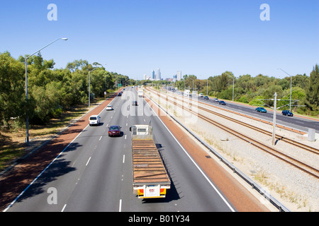 Verkehr auf der Mitchell-Autobahn in Richtung Perth, aus Wolkenkratzer sind in der Ferne. Schienen sind zwischen den Straßen. Stockfoto