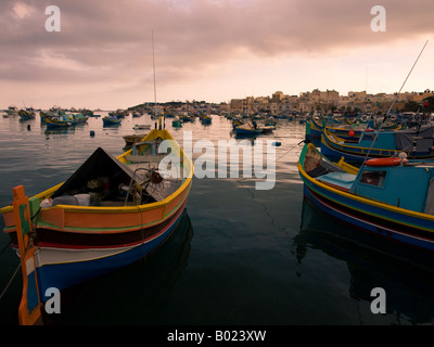 Ein Fischer und bunte Luzzu Fischereifahrzeuge am Ende des Tages in Marsaxlokk, Malta. Stockfoto