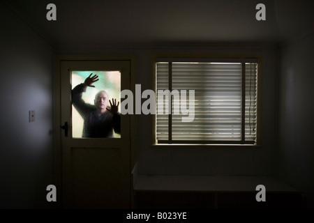 Mann sieht in Raum durch Milchglas Fensterscheibe an Tür neben Fenster mit Rollo Stockfoto
