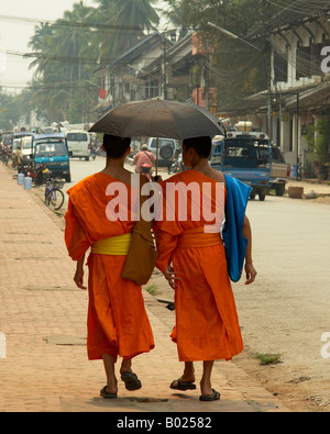 Zwei buddhistische Mönche zu Fuß mit einem Regenschirm über die Hauptstraße in Luang Prabang Loas Stockfoto