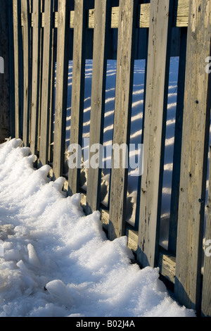 Hölzerne Lattenzaun im Schnee. Stockfoto