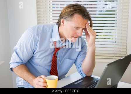 A, müde und gestresst Geschäftsmann schaut auf seinem Laptop befürchtete das Schlimmste. Stockfoto