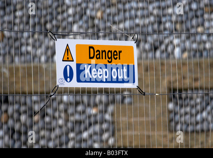 Halten, blau & gelben Warnschild auf einem umzäunten Baustelle mit Flint Wand & Steingebäude im Hintergrund Stockfoto