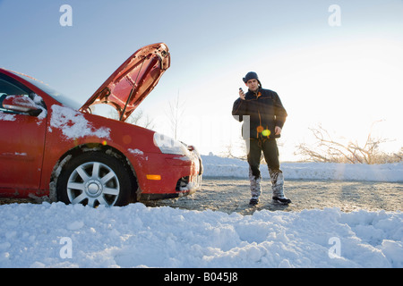 Man spricht am Handy neben Auto mit Haube im Winter Stockfoto