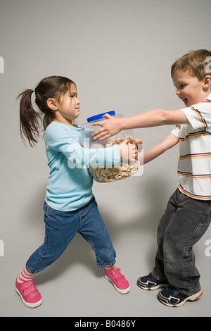 Ein Junge und ein Mädchen kämpfen über eine Dose Kekse Stockfoto