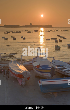 Kleine Fischerboote am Playa De La Caleta Backdropped von Castillo de San Sebastian bei Sonnenuntergang in der Stadt Cadiz Stockfoto