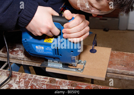 junger Mann im Hause ein Stück Holz mit einer Stichsäge schneiden Stockfoto