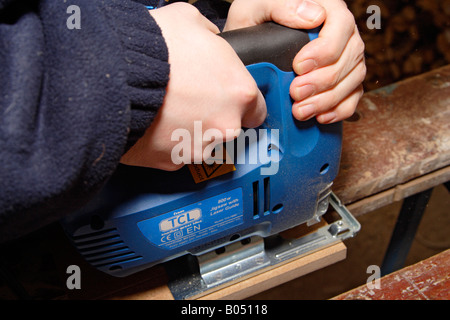 junger Mannhände hautnah ein Stück Holz mit einer Stichsäge schneiden Stockfoto