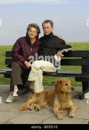 Hovawart (Canis Lupus F. Familiaris), älteres Paar mit Hund auf Bank sitzend Stockfoto