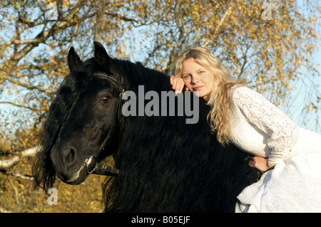 inländische Pferd (Equus Przewalskii F. Caballus), blonde Frau im weißen Kleid auf schwarzes Pferd Stockfoto