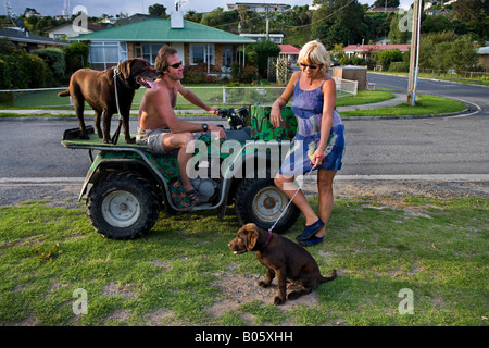 Blonde Frau im Gespräch mit einem Mann auf ein geländegängiges Fahrzeug, Spaziergang mit seinem Hund in einem Suburban Straße in Omokoroa, Neuseeland Stockfoto