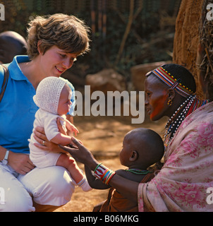 Eine Europäerin und schwarzen Masai Tribeswoman in traditioneller Kleidung stellen ihre Babys einander im Massai-Dorf Kenia Stockfoto