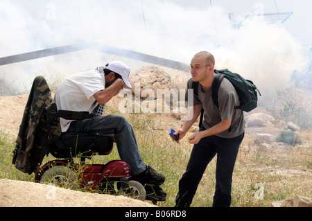 Ein behinderter Palästinenser in seinem Rollstuhl, die Teilnahme an einer Protestkundgebung gegen Israel inmitten von Tränengas, geholfen durch einen Ausländer Stockfoto