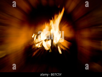 Ein Holzfeuer mit hellen Flammen brennen in einen Kamin. Ein Zoom-Effekt wird verwendet, um eine abstrakte Unschärfe rund um den Kamin zu schaffen. Stockfoto