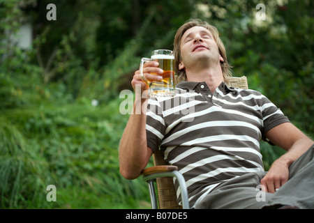 Mann hält ein Glas Bier in einem Liegestuhl sitzen Stockfoto
