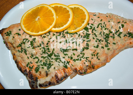 Gegrillte ohne Knochen wild Pacific Coho Lachs-Filet mit Orangenscheibe und gehackten Schnittlauch garniert auf einem großen Teller Stockfoto