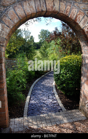 EIN STEIN BOGEN FÜHRT ZU EINEM GARTENWEG GELEGT MIT SCHIEFER SCHERBEN UND EINGEFASST MIT GRANIT PFLASTERSTEINE Stockfoto