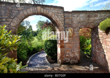 EIN STEIN BOGEN FÜHRT ZU EINEM GARTENWEG GELEGT MIT SCHIEFER SCHERBEN UND EINGEFASST MIT GRANIT PFLASTERSTEINE Stockfoto