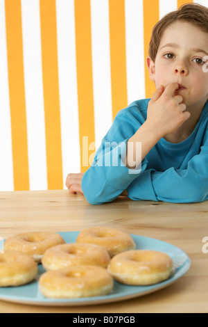 Junge sitzt vor ein paar donuts Stockfoto