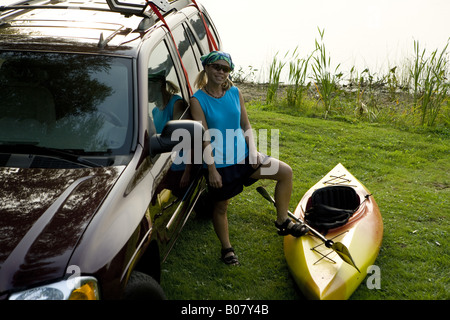 Frau mit Kajak neben GMC Envoy am See Stockfoto