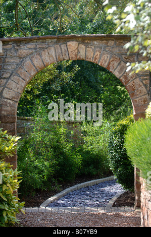 EIN STEIN BOGEN FÜHRT ZU EINEM GARTENWEG GELEGT MIT SCHIEFER SCHERBEN UND EINGEFASST MIT GRANIT PFLASTERSTEINE Stockfoto