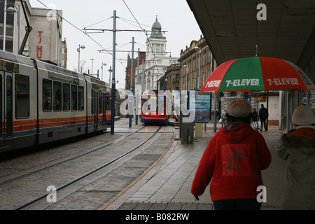 Fußgänger, betrachten einige Straßenbahnen in Sheffield Stadtzentrum halten einen Regenschirm Stockfoto