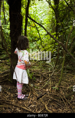 Mädchen im Alter von vier Ständen mit einer Hand an einem Baum allein im Wald. Neuseeland Stockfoto