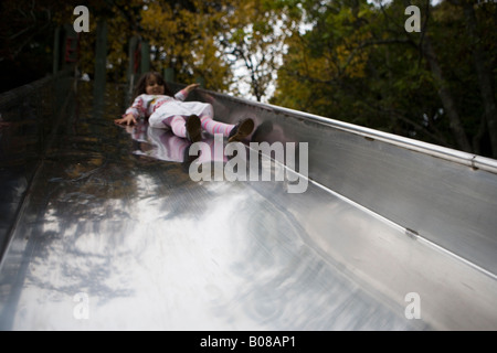 Mädchen im Alter von vier Jahren Folien Stahl Rutsche in einen Abenteuerspielplatz Stockfoto