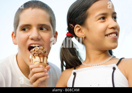 Preteen Mädchen Eistüte zu halten, während ein Junge einen Bissen nimmt Stockfoto