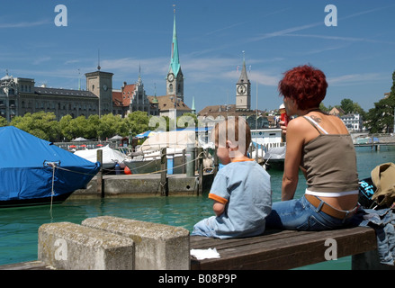 Blick über die Limmat Fraumünster und St. Peter Church; eine Mutter mit ihrem Sohn sitzen auf einer Bank im Vordergrund, Großbrit Stockfoto