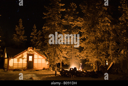 Beleuchtete Hütte, Elch Geweih montiert über der Tür, Lagerfeuer in einem Wald im Winter, Yukon Territorium, Kanada Stockfoto