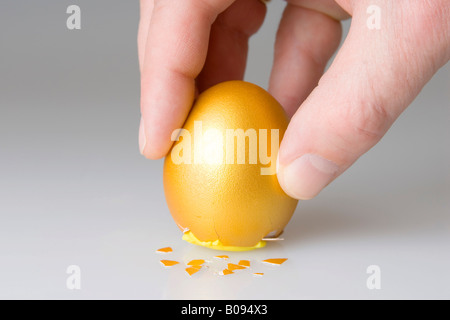 Ei des Kolumbus, Hand Positionierung goldenes Ei auf dem rissigen Boden Stockfoto