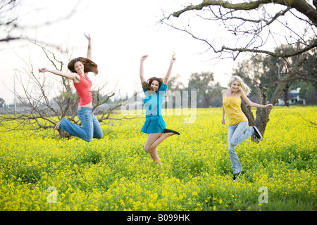 Drei junge Frauen Lächeln auf den Lippen und in einem gelben Feld Senf Pflanzen springen. Stockfoto