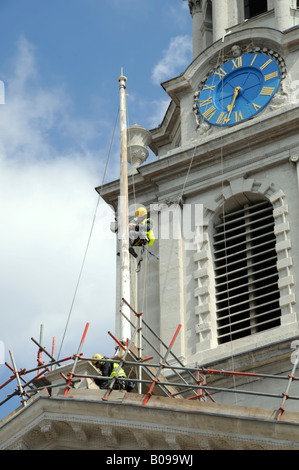 Mann arbeitet von Stuhl Wiege am Fahnenmast auf Kirchendach Malerei Holz Vorbereitung umfasst Uhrturm Stockfoto