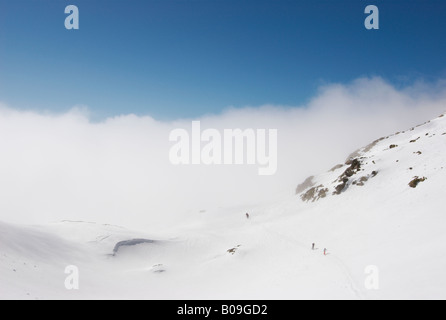 Gruppe von Skifahrern nähert sich Col Cicle an einem sonnigen Wintertag über den Wolken, Les Contamines-Montjoie, Frankreich Stockfoto