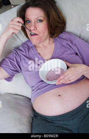 Schwangere Frau sitzend auf einem Stuhl Essen Joghurt Modell veröffentlicht Stockfoto
