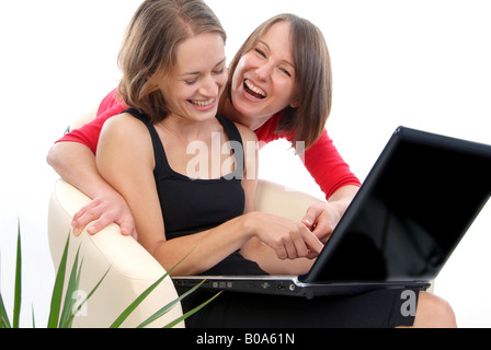 zwei fröhliche junge Frauen mit einem Laptop; man zeigt etwas auf dem Bildschirm zu ihrer Freundin Stockfoto