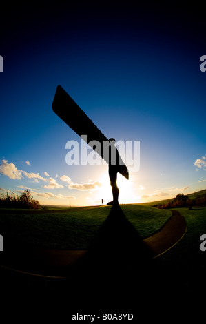 Eine Figur mit ausgestreckten Armen am Fuß des Engels des Nordens in Gateshead. Vor einem blauen Himmel bei Sonnenuntergang gesehen Stockfoto