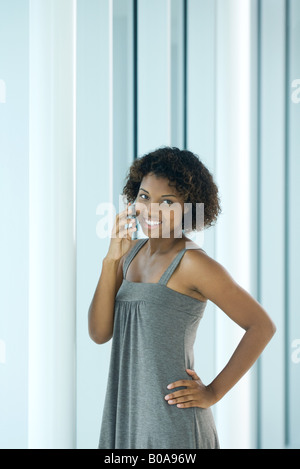 Junge Frau stehend mit Hand auf Hüfte, mit Handy, Lächeln Stockfoto