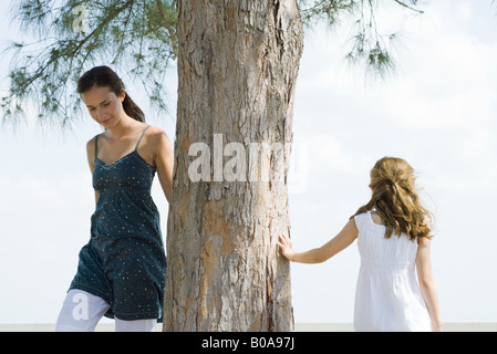 Zwei Schwestern herumlaufen Baumstamm, kleines Mädchen Baum mit der Hand berühren Stockfoto