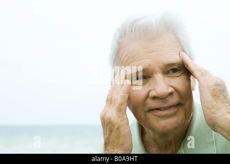 Ältere Mann mit den Fingern seitlich des Kopfes, Lächeln, wegschauen Stockfoto