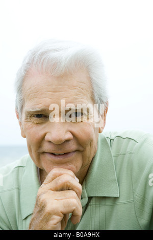 Ältere Mann mit Hand unter Kinn, lächelnd in die Kamera, Porträt Stockfoto