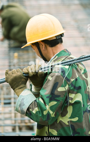 Bauarbeiter, tragen, Tarnung und Schutzhelm tragen Metallstab auf Schulter, Seitenansicht Stockfoto