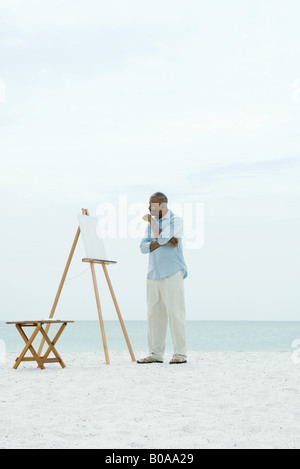 Senior woman steht man vor der leeren Leinwand am Strand, mit Pinsel Stockfoto