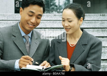 Männliche und weibliche Geschäftspartnern Blick auf Agenda zusammen, Lächeln, Mann, der Stift hält Stockfoto